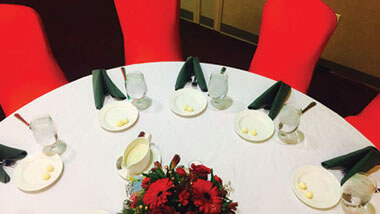 Red chairs surround a circular table covered in a white table cloth and set with black napkins and white plates complete with a red gerbera daisy centerpiece inside the banquet space at Hollywood Casino in St. Louis, Missouri.