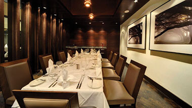 A long table set surrounded by tan and brown chairs and set with white linens inside Final Cut Steakhouse at Hollywood Casino in St. Louis, Missouri.