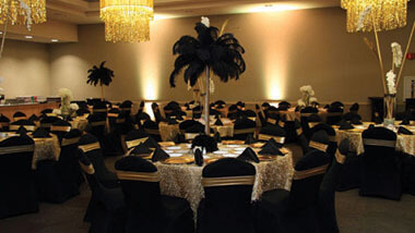 Chandeliers hang over tables covered in white lace with tall, feathered centerpieces inside Hollywood Casino St. Louis' banquet space.