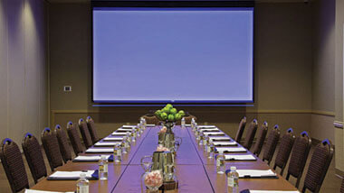 Chairs lined up on either side of a long board room table with a large projector screen on the wall.