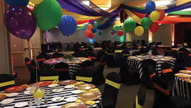 Multi-colored material is draped from the ceiling above multi-colored balloons and several round tables with black-and-white striped table cloths inside the banquet space at Hollywood Casino in St. Louis, Missouri.
