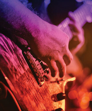 Hands strumming the strings of an electric guitar with a purple and orange color overlay.