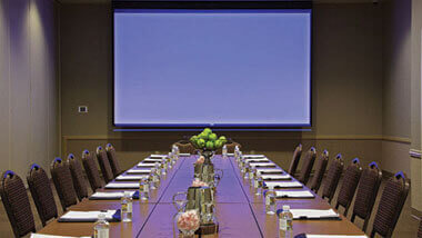 A boardroom table set up for a meeting with a large projection screen on the wall.