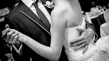 Close-up black-and-white picture of the arms and torsos of a groom and bride dancing.
