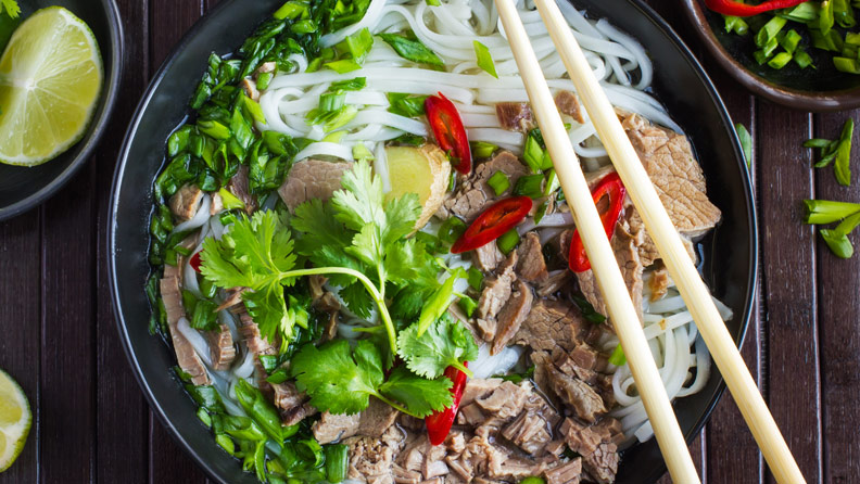 beef pho on wooden background with lime and cilantro